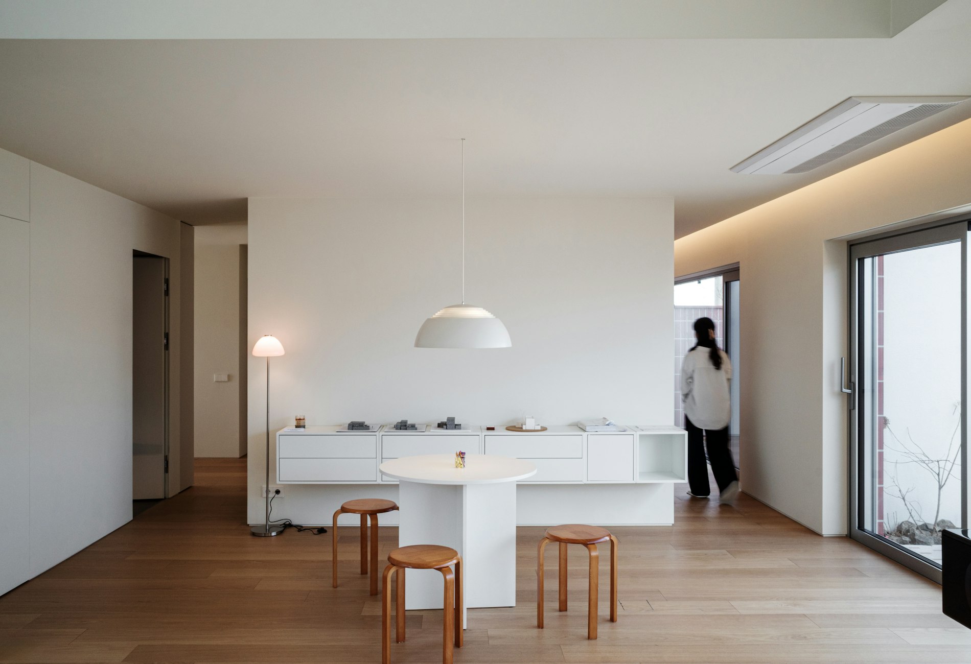 Interior nórdico con mobiliario modular blanco, mesa redonda y taburetes de madera bañados por luz natural